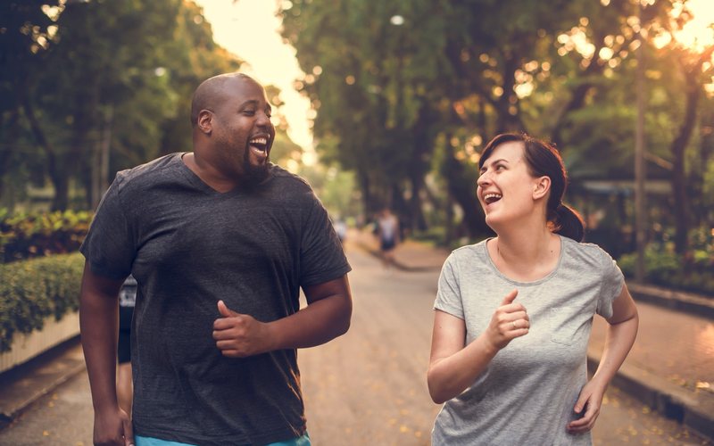A couple jogging together along a tree-lined path at sunset.